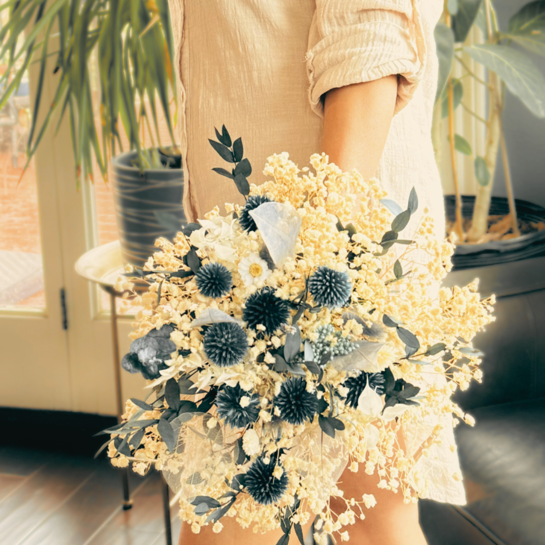 A woman holding a blue themed dried flowers bouquet next to her leg