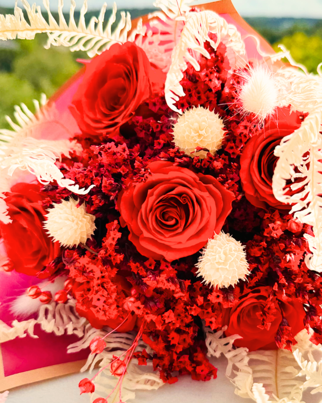 A vibrant red rose bouquet laying on a flat surface made with dried flowers